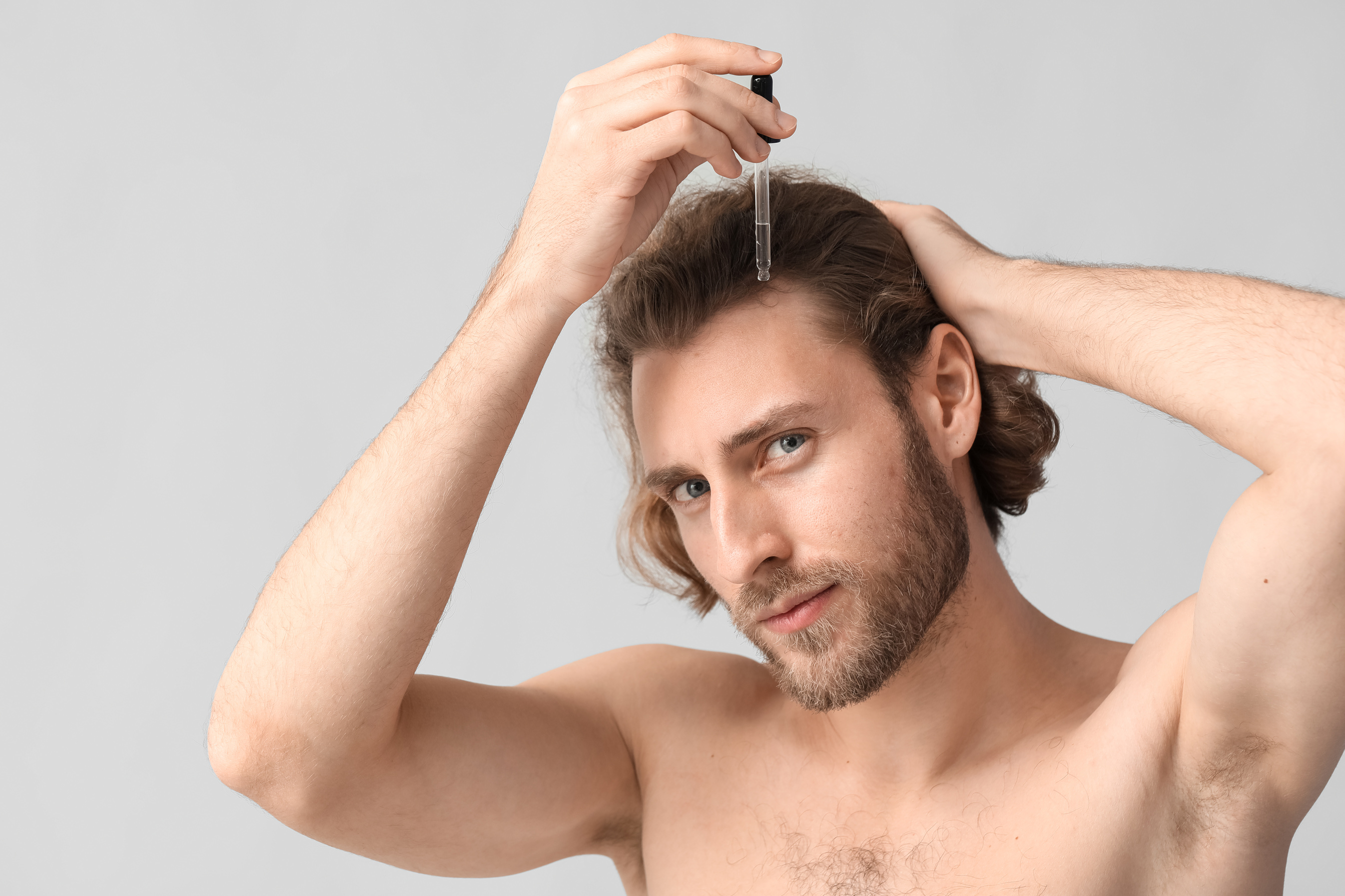 Young Man Using Serum for Hair Growth on Grey Background